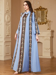 Detail of ethnic embroidery and gold geometric patterns on a light blue V-neck long dress