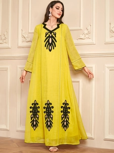 Détail de la broderie ethnique noire sur une robe longue jaune à manches longues