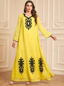 Détails de broderies ethniques noires sur une robe longue jaune à manches longues