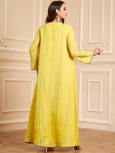 Détail de broderie foncée sur une robe maxi jaune vif à manches longues et aspect lin