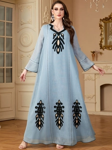 Détail d'une robe maxi bleu clair avec broderies dorées et noires sur le col et l'ourlet