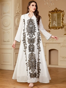 Broderie détaillée noire et dorée sur une élégante robe longue blanche à manches