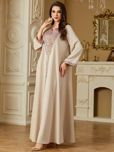 Detail showing colorful geometric embroidery on the neckline of a beige kaftan dress