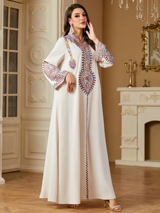 Close-up of colorful heavy embroidery patterns on white bohemian kaftan dress sleeves