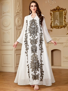 Détail de broderie dorée élégante sur une robe longue blanche à manches longues