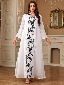 Detail of elegant white long dress showing intricate black vine embroidery and fabric texture