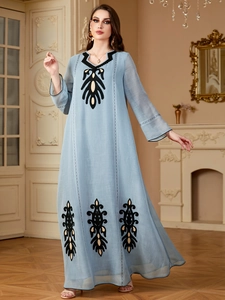 Détail de robe longue bleu clair à manches longues avec motifs de broderie noirs et dorés