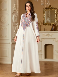 Detail der farbenfrohen Ethno-Stickerei und Pailletten auf weißem Langarm-Maxikleid
