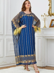 Détail de la robe longue bleu marine avec broderie dorée et poignets en plumes jaunes