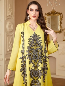 Détail de broderie de paillettes noires et grises sur une robe kaftan en lin jaune