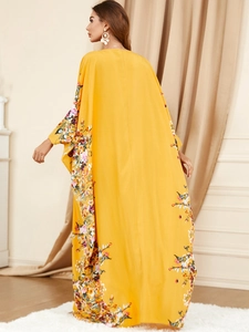 Détail d'un caftan jaune ample avec imprimé floral et manches chauve-souris élégantes