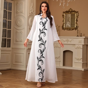 Elegant white kaftan dress with black embroidery and long sleeves in a luxury room