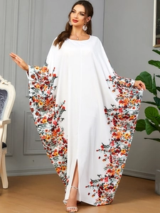 Détail d'une robe caftan blanche avec motifs floraux rouges et orange sur manches chauve-souris