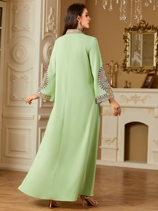 Detail of ethnic embroidery on the neckline and cuffs of a light green long maxi dress
