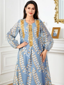 Détail de la broderie à paillettes dorées sur l'encolure d'une robe bleue à manches