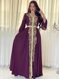 Détail de la broderie florale dorée et ceinture à pompons sur une robe caftan violet foncé