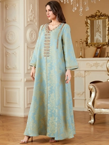 Macro detail of intricate gold floral embroidery and red beadwork on light blue Kaftan