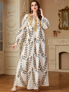Détails de broderie de paillettes dorées sur la robe à fleurs blanche à manches longues