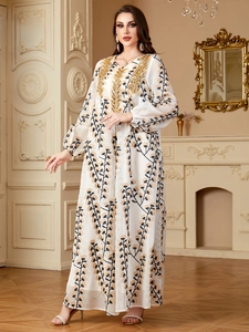 Détail de broderie de paillettes dorées sur l'encolure en V d'une robe caftan blanche