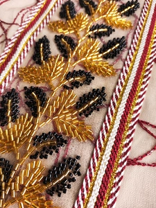 Macro detail of intricate gold beadwork and leaf embroidery on beige mesh fabric