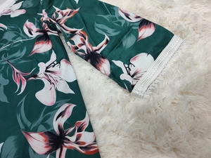 Détail d'une robe fleurie verte avec poignets en dentelle blanche et imprimé de lys