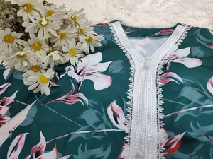 Détail de robe fleurie vert foncé avec décolleté en V en dentelle blanche et bouton en tissu