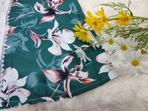 Détail de robe en satin vert foncé avec imprimé de lys et bordure en dentelle blanche