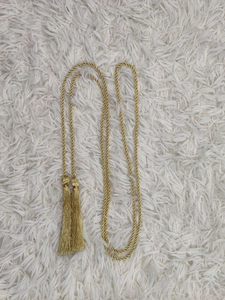 Golden woven braided belt cord with elegant tassels on white plush background