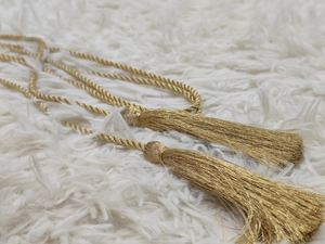 Detail of golden tassel pendants with twisted cord weave on a white plush background