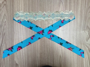 Detail of blue floral fabric belt with pink roses and golden lace on wood background