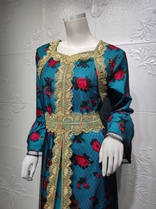 Detail of teal kaftan dress featuring gold lace embroidery and red floral prints