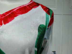 Vue détaillée du tissu satiné lisse avec imprimé feuilles tropicales rouge et vert