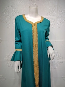 Detail of dark green kaftan dress with golden fringe trim and elegant ruffle sleeves