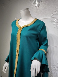 Detail of emerald green kaftan dress featuring gold embroidered trim and ruffle sleeves