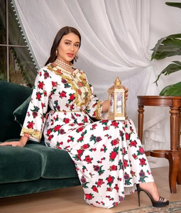 Detail of white kaftan dress with red floral print and gold embroidery on velvet sofa