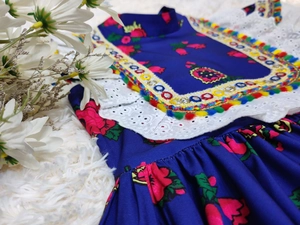 Detailed close-up of blue girl dress with floral patterns, white lace and pom poms