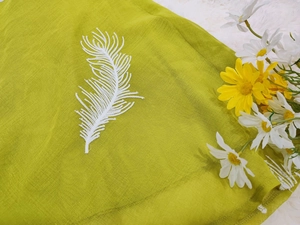 Detailed embroidery of white feathers on green fabric with high-quality stitching texture