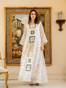 Detailed embroidery of colorful square sequins on a white flowy maxi dress with gold trims