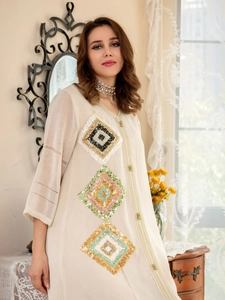 Détail de broderie de paillettes et manches rayées ajourées sur robe longue crème