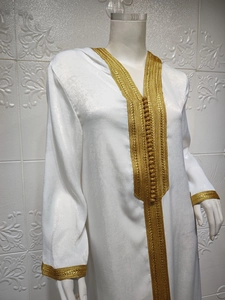Detail of white kaftan robe featuring intricate golden lace embroidery and braided buttons