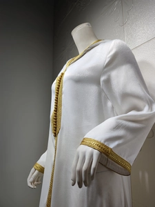 Macro shot of intricate golden embroidery on the neck and front of the white kaftan dress