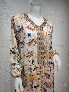 Détail de broderies dorées ethniques sur une robe caftan en soie imprimée