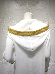 Detail of white hooded dress featuring intricate gold lace trim on the hood and cuffs