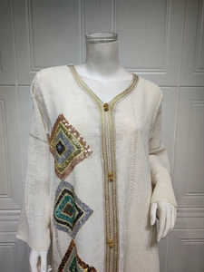 Détail des motifs en paillettes et du col en V avec perles dorées sur la robe beige