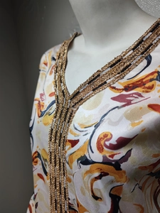 Détail du col en V avec paillettes argentées et chaîne en métal sur l'abaya imprimée