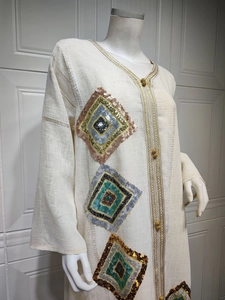 Détail des motifs de losanges à paillettes et bordures dorées sur cette robe caftan crème