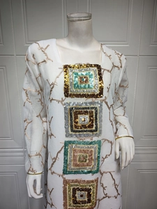 Detail of white embroidered tunic dress featuring colorful sequin squares and golden branches
