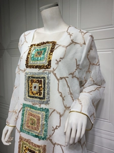 Detail of white dress featuring gold branch embroidery and four colored sequin squares