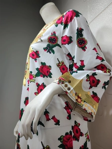Detail of floral kaftan dress featuring golden sequin trim on white lightweight fabric