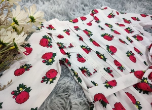 Détail de robe bébé blanche avec imprimé floral rouge et bordure en dentelle ajourée
